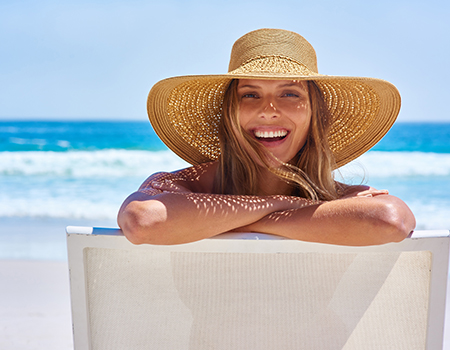Woman with a sunhat is sitting in a chair at the beach. 
