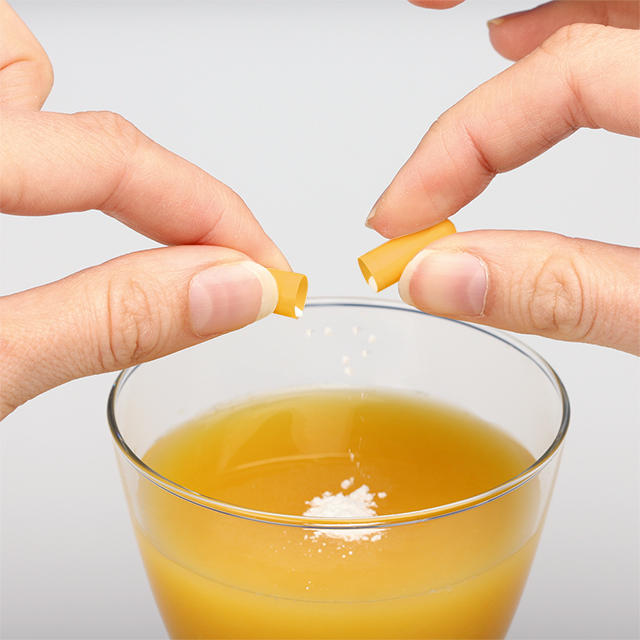 A capsule is pulled apart and the contents is emptied into a glass of juice.